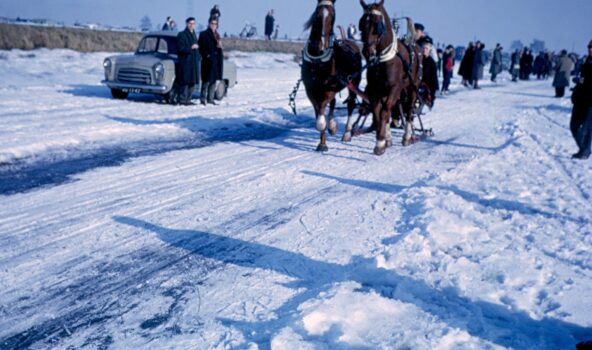 Foto uit 1963 met daarop paarden met een arrenslee op het ijs in Kinderdijk. Ze zijn omringt door veel mensen op het ijs en staat zelfs een auto op het ijs.