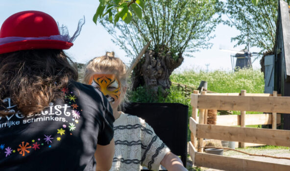 Een kind dat op het molenerf in Kinderdijk geschminkt wordt met op de achtergrond een molen.